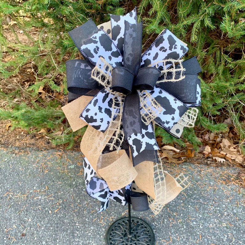 Black and White Cow Bow on a wreath stand photographed outdoors to give a natural light perspective.  The wreath stand is for display only and not for sale. Refer to the listing description for further bow details.