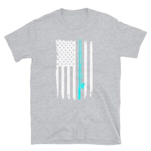 May include: A gray t-shirt featuring a distressed American flag design with a light blue fishing rod graphic. The flag has white stripes and a field of white stars. The fishing rod is vertically centered.