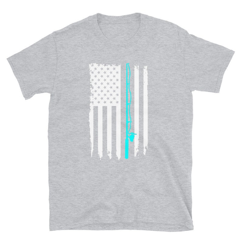 May include: A gray t-shirt featuring a distressed American flag design with a light blue fishing rod graphic. The flag has white stripes and a field of white stars. The fishing rod is vertically centered.