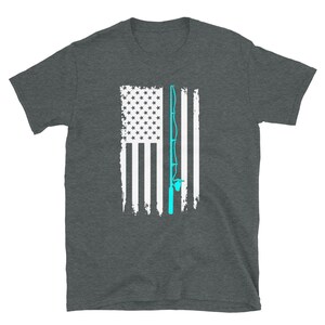 May include: Dark gray t-shirt featuring a distressed American flag design with a light blue fishing rod overlay. The flag has white stripes and a field of white stars. The shirt is made of a soft material.