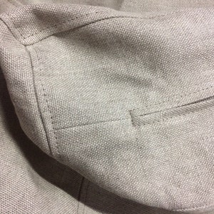 May include: Close-up of a beige fabric with a seam running along the edge. The fabric has a textured, woven appearance.