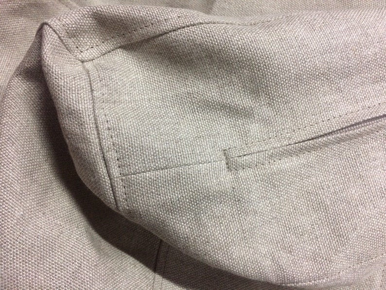May include: Close-up of a beige fabric with a seam running along the edge. The fabric has a textured, woven appearance.