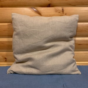 May include: A plain, beige linen pillow with a zipper closure. The pillow is sitting on a blue surface.