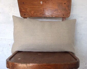 May include: A light beige linen pillow resting on a wooden chair with a worn wooden back.
