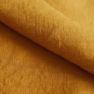 May include: Close-up of a folded piece of mustard yellow linen fabric. The fabric has a textured, woven appearance.