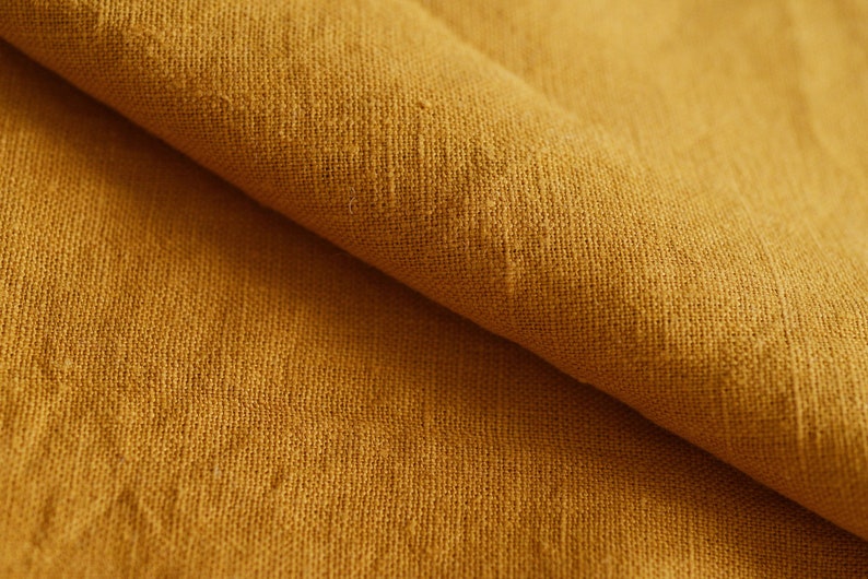 May include: Close-up of a folded piece of mustard yellow linen fabric. The fabric has a textured, woven appearance.