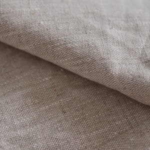 May include: Close-up of a natural linen fabric with a textured weave. The fabric is a light beige color and has a soft, natural feel.