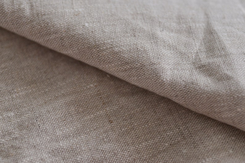 May include: Close-up of a natural linen fabric with a textured weave. The fabric is a light beige color and has a soft, natural feel.
