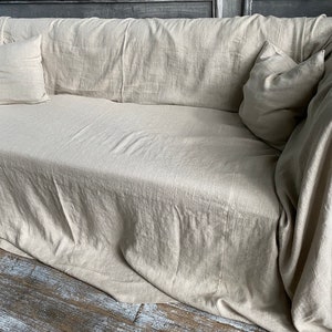 May include: A beige linen sofa with two pillows, one on each end. The sofa is covered in a beige linen throw blanket.