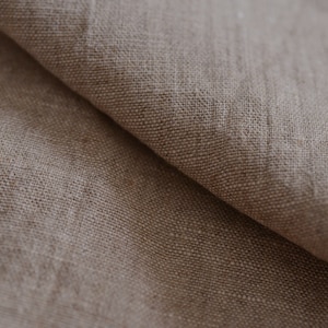 May include: Close-up of a natural linen fabric with a textured, woven pattern. The fabric is a light brown color and has a soft, natural feel.