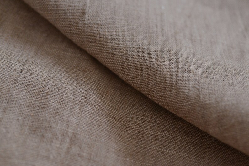 May include: Close-up of a natural linen fabric with a textured, woven pattern. The fabric is a light brown color and has a soft, natural feel.