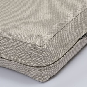 May include: A beige cushion with a zipper closure. The cushion is made of a textured fabric.