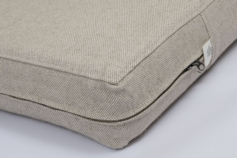 May include: A beige cushion with a zipper closure. The cushion is made of a textured fabric.