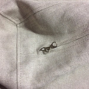 May include: A close-up of a zipper on a light gray canvas bag. The zipper is made of metal and has a silver finish.