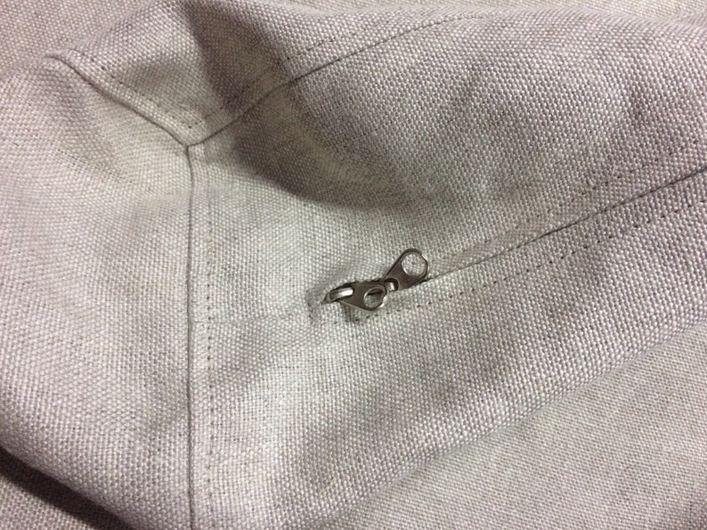 May include: A close-up of a zipper on a light gray canvas bag. The zipper is made of metal and has a silver finish.