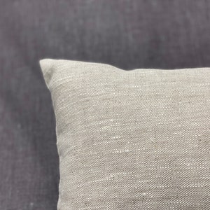 May include: A close-up of a light beige linen pillow with a textured surface.