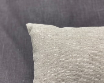 May include: A close-up of a light beige linen pillow with a textured surface.