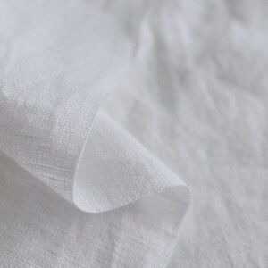 May include: Close-up of a white linen fabric with a soft, textured surface. The fabric is folded and draped, creating a smooth, flowing curve.