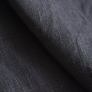 May include: Close-up of a dark gray fabric with a textured weave. The fabric is folded in half, showing the texture of the material.