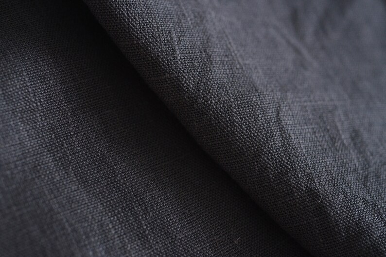 May include: Close-up of a dark gray fabric with a textured weave. The fabric is folded in half, showing the texture of the material.