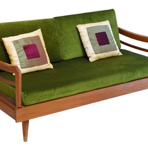 May include: A green velvet sofa with wooden arms and legs. The sofa has two pillows with a patterned fabric.