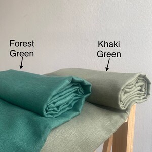 May include: Two fabric swatches, one forest green and one khaki green, rolled up and displayed on a wooden surface.