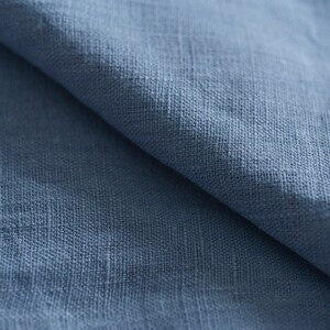 May include: Close-up of a blue linen fabric with a textured weave. The fabric is folded in half, showing the soft, natural texture.
