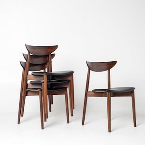 May include: A set of mid-century modern dining chairs. The chairs have dark brown wooden frames with curved backs and black leather seats. One chair stands alone, while the others are stacked together. The chairs are set against a white background.