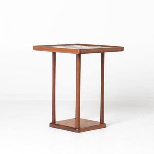 May include: A square side table constructed from medium-toned wood, featuring four slender, straight legs that connect a flat top surface to a smaller square base. The tabletop surface displays a tiled pattern with white and grey geometric accents.