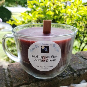 K&ouml;nnte beinhalten: Eine Kerze in einem durchsichtigen Glasbecher mit dunkelrotem Wachs und einem Holzdocht. Die Kerze ist mit "Hot Apple Pie/Coffee Break" von Butterfly Dreams Boutique beschriftet. Die Kerze ist 454 Gramm.