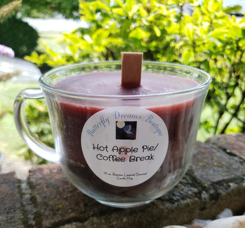 K&ouml;nnte beinhalten: Eine Kerze in einem durchsichtigen Glasbecher mit dunkelrotem Wachs und einem Holzdocht. Die Kerze ist mit "Hot Apple Pie/Coffee Break" von Butterfly Dreams Boutique beschriftet. Die Kerze ist 454 Gramm.