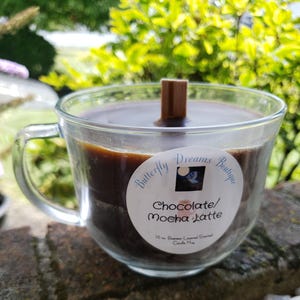 K&ouml;nnte beinhalten: Eine klare, becherf&ouml;rmige Kerze aus Glas, gef&uuml;llt mit dunkelbraunem Wachs. Die Kerze hat einen Holzdocht und ein Etikett mit der Aufschrift "Chocolate/Mocha Latte" von Butterfly Dreams Boutique. Die Kerze ist 283 Gramm.