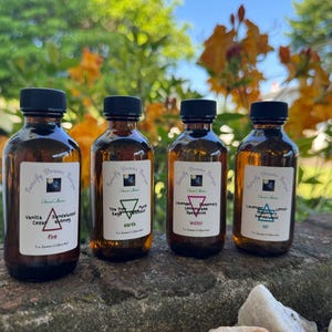 Könnte beinhalten: Vier braune Glasflaschen mit schwarzen Deckeln stehen auf einer Steinoberfläche. Jede Flasche hat ein weißes Etikett mit Text und einem geometrischen Symbol. Die Etiketten lauten: Vanille, Zeder, Sandelholz, Teebaum, Salbei, Myrrhe, Lavendel, Rosmarin, Minze und Lavendel, Zitrone, Sandelholz.
