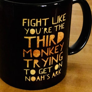 May include: Black coffee mug with a gold design that reads "Fight like you're the third monkey trying to get on Noah's ark."