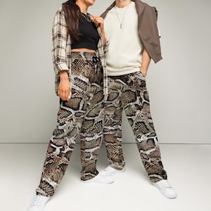 May include: Two people wearing matching snake print pants. The woman is wearing a plaid shirt and the man is wearing a white shirt with a brown jacket.