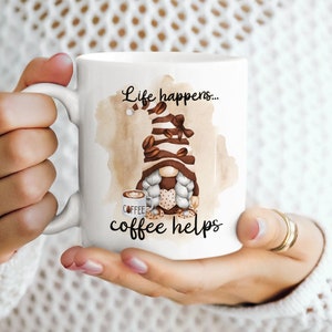 May include: White ceramic coffee mug with a brown and white gnome illustration. The mug has the text "Life happens... coffee helps" printed on it.