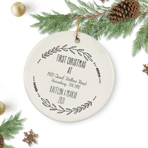 May include: White ceramic Christmas ornament with black text that reads "First Christmas at 1420 Quail Hollow Road Harrisburg, PA 17112 Kaitlyn & Mario 2021" surrounded by a wreath of black leaves.