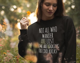 May include: A black sweatshirt with the text "Not all who wander are lost. Some are looking for cool rocks." printed in white.