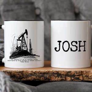 May include: Two white ceramic mugs with black handles. One mug features a black and white illustration of an oil rig with the quote "Our business is one of constant crisis, interrupted by brief periods of intense success." - Jimmy Harris. The other mug has the name "JOSH" printed in black.