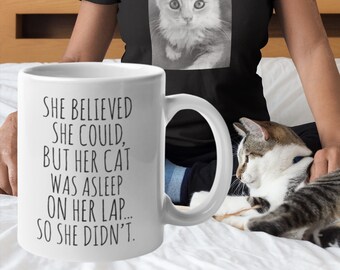 May include: White ceramic mug with black text that reads "She believed she could, but her cat was asleep on her lap... so she didn't."