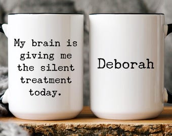 Pode incluir: Duas canecas de cerâmica brancas com alças e bordas pretas. Uma caneca diz "My brain is giving me the silent treatment today." A outra caneca é impressa com o nome "Deborah."