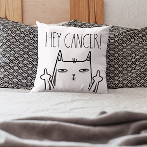 May include: White throw pillow with a black and white illustration of a cat giving the middle finger with the text "Hey Cancer!" printed on it.