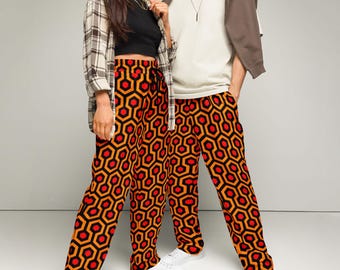 May include: Two people wearing matching pants with a geometric pattern in orange, red, and black. The pants have a wide leg and a drawstring waist.