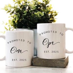May include: Two white ceramic mugs with black text. The mug on the left says "Promoted to Oma Est. 2025". The mug on the right says "Promoted to Opa Est. 2025".