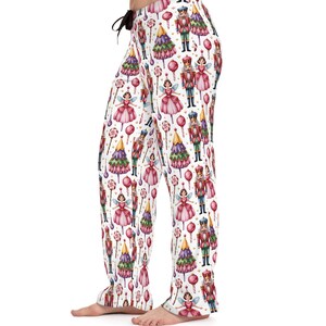 May include: White pajama pants with a repeating pattern of a fairy, nutcracker, Christmas tree, and lollipop design. The pants have a drawstring waist and a relaxed fit, perfect for lounging.