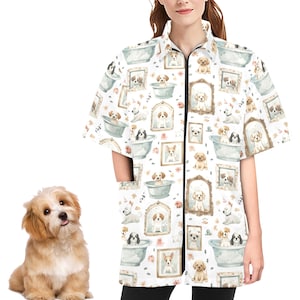May include: A white short-sleeved zip-up grooming smock featuring a repeating pattern of watercolor-style illustrations of dogs in bathtubs and framed portraits. The smock has a black zipper and pockets.
