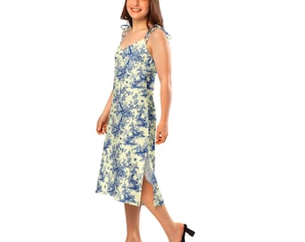 May include: A light yellow midi dress with a blue toile print. The dress features adjustable tie straps, a button-down front, and a side slit. The model is wearing black heeled sandals.