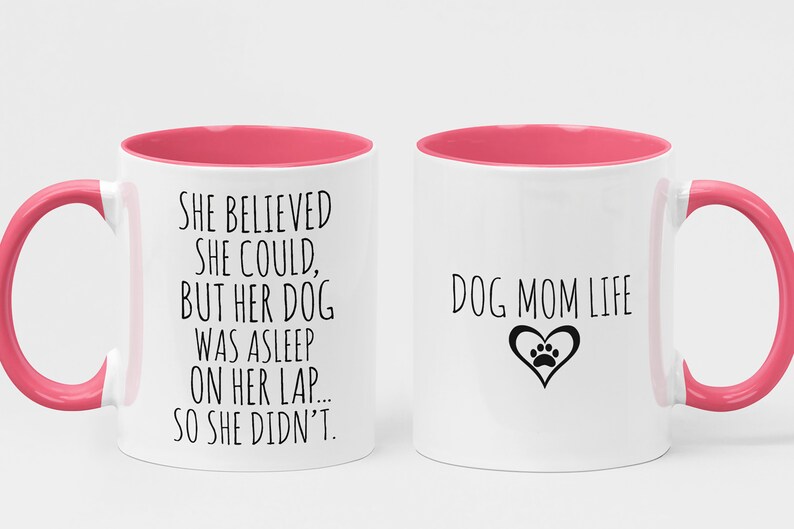Op de afbeelding: Twee witte koffiemokken met roze accenten. Op de ene mok staat "She believed she could, but her dog was asleep on her lap... so she didn't." Op de andere mok staat "Dog Mom Life" met een hart en een pootprint.