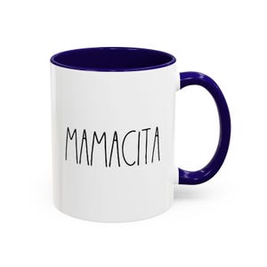 May include: White ceramic mug with a navy blue interior and handle. The word "MAMACITA" is printed in black, handwritten-style lettering on the front of the mug. A simple, yet stylish design.