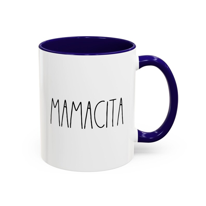 May include: White ceramic mug with a navy blue interior and handle. The word "MAMACITA" is printed in black, handwritten-style lettering on the front of the mug. A simple, yet stylish design.